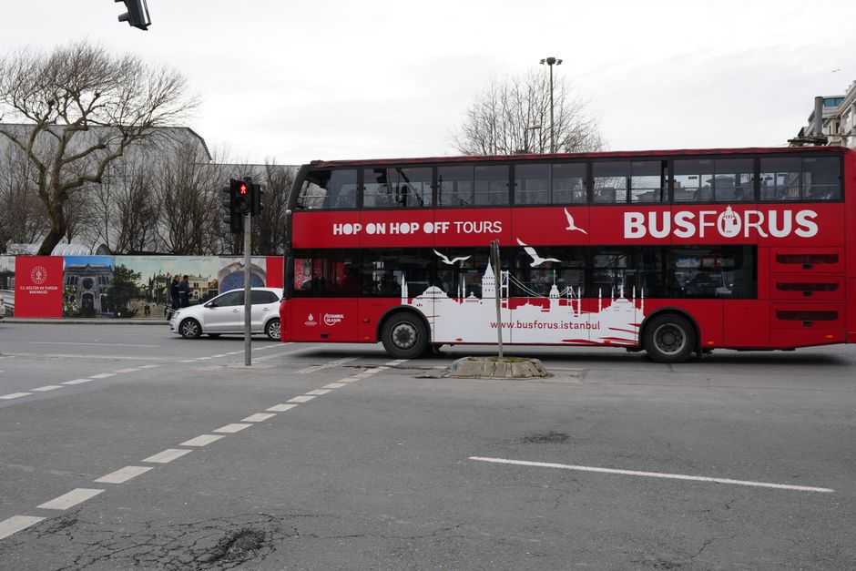 A red double-decker hop-on hop-off tour bus driving past iconic landmarks in London, Great Britain