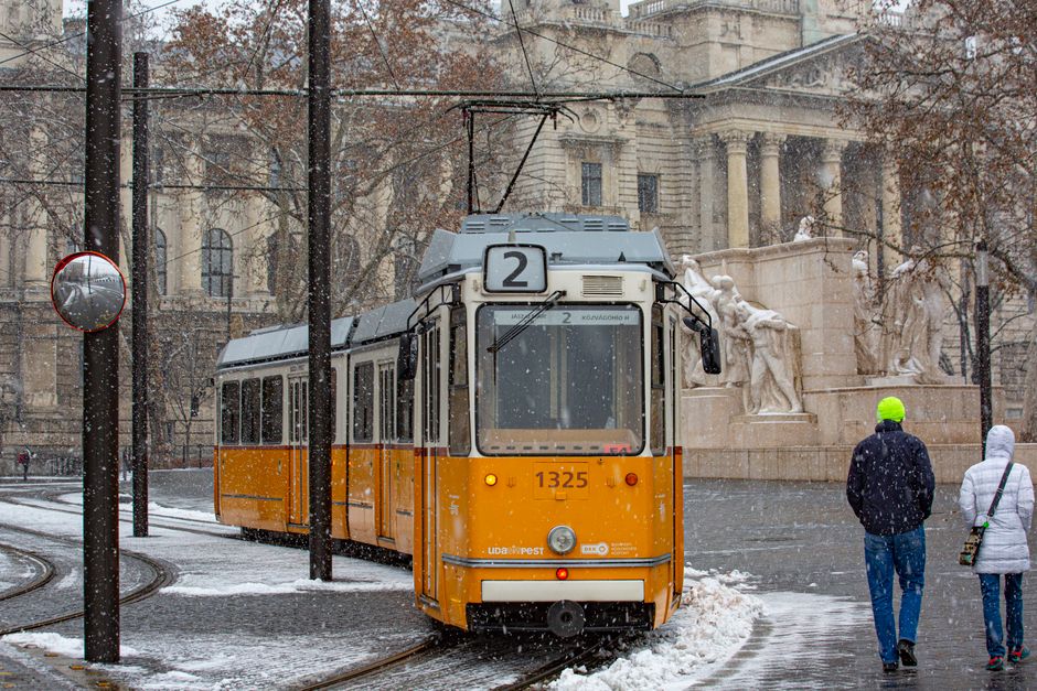 A yellow tram moving through a bustling street in Budapest, Hungary, with historic buildings in the background.