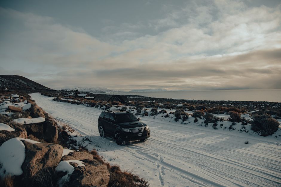A 4x4 rental car driving on a gravel road through a vast, dramatic Icelandic landscape