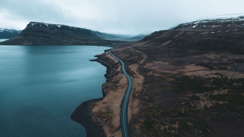 A car driving along the scenic Ring Road in Iceland with mountains and a vast landscape in the background