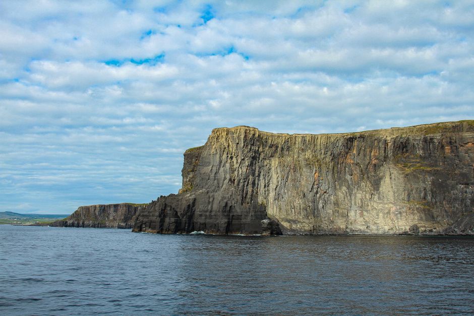 A tour bus parked near the majestic Cliffs of Moher in Ireland, with tourists admiring the dramatic coastal views.