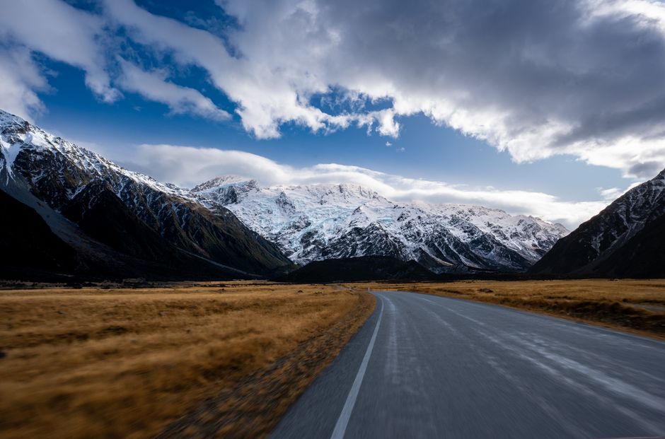 A rental car driving along a scenic coastal road in New Zealand, showcasing the freedom of a road trip