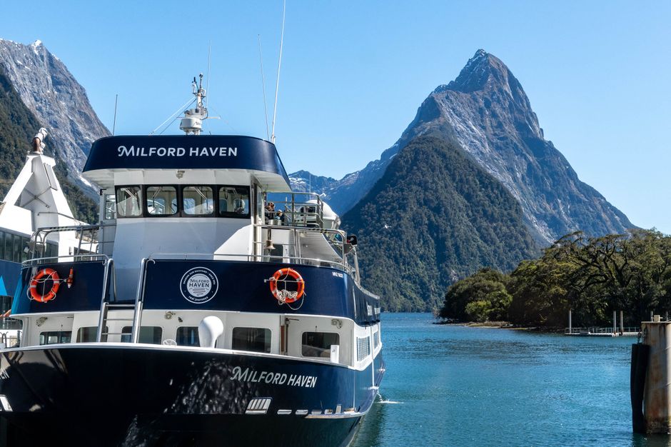 A scenic cruise boat navigating the majestic fjords of Milford Sound, New Zealand, with towering cliffs and waterfalls