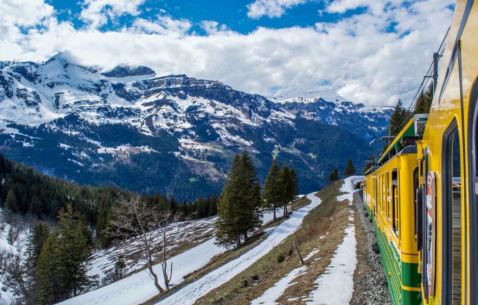 A panoramic view of a red train winding through the Swiss Alps, showcasing a classic Switzerland day trip experience.