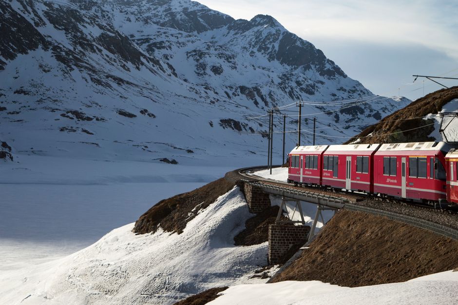 Red train traveling through a stunning mountain landscape in Switzerland