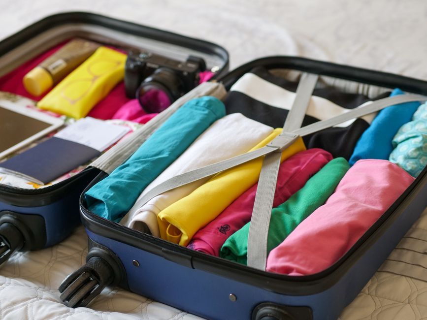 A person packing a suitcase with items for a trip to the UAE, including a headscarf and lightweight clothes.