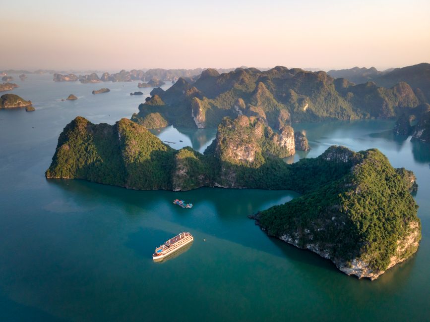 Traditional junk boat cruising through the limestone karsts of Ha Long Bay, Vietnam at sunset