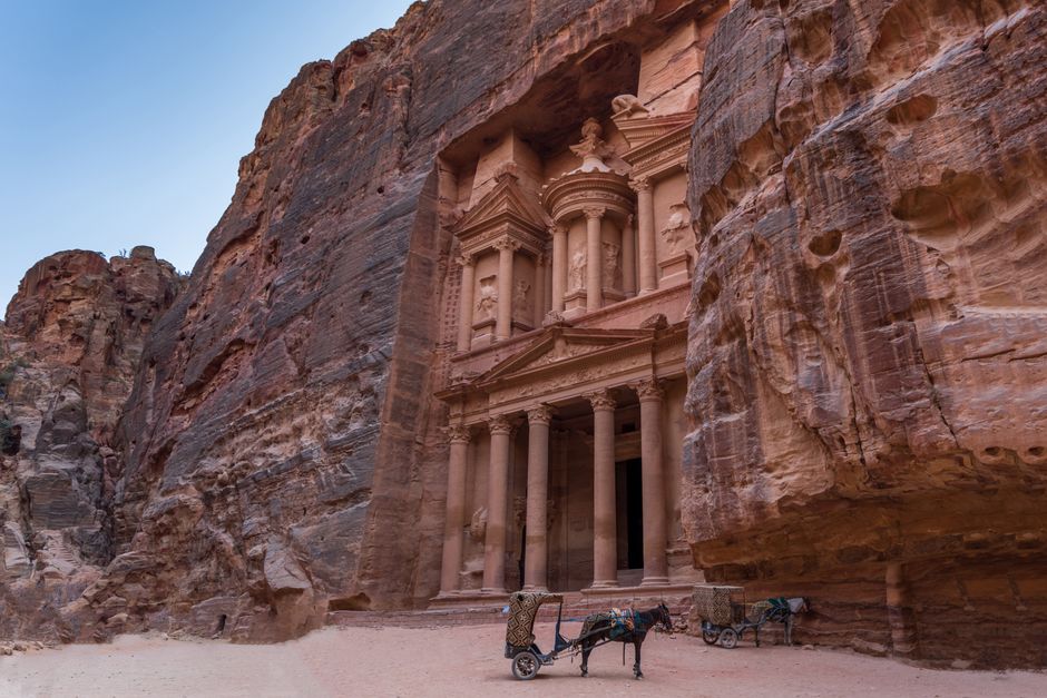 A white rental car parked with the ancient city of Petra, Jordan in the background, ready for a road trip.