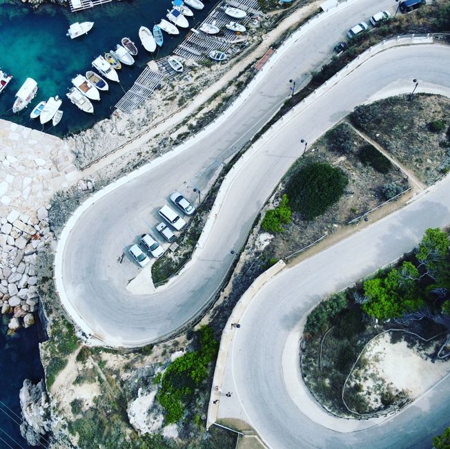 A rental car driving along a scenic coastal road in Malta with the Mediterranean Sea in the background