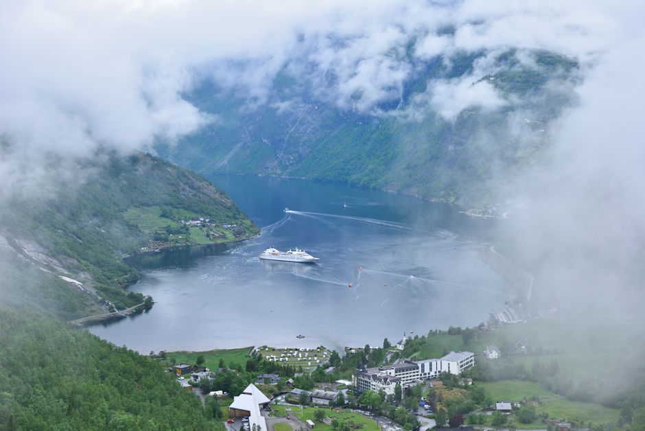 A scenic cruise boat navigating the stunning Geirangerfjord in Norway, surrounded by towering cliffs and waterfalls.