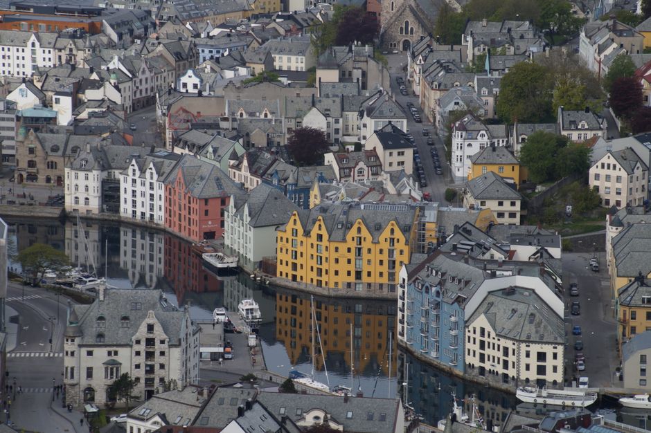 A bustling street scene in a Norwegian town, showcasing daily life and local businesses, hinting at travel costs.