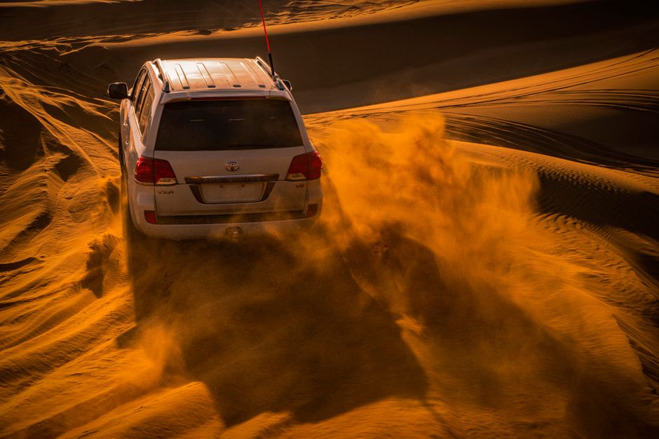 A white Toyota Land Cruiser 4x4 driving on a winding road through the rugged Hajar Mountains in Oman, showcasing the adventurous spirit of Omani travel.