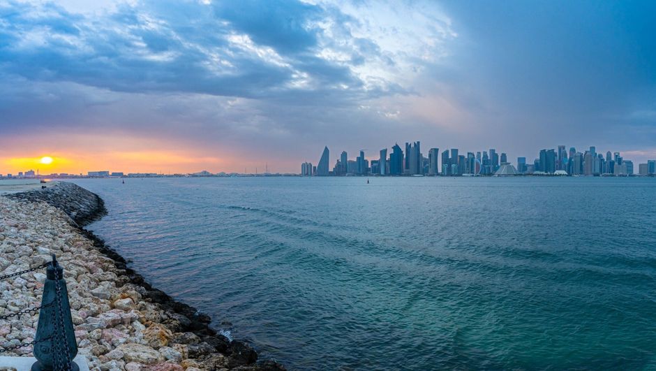 Doha skyline at sunset with modern buildings and traditional dhow boats in Qatar