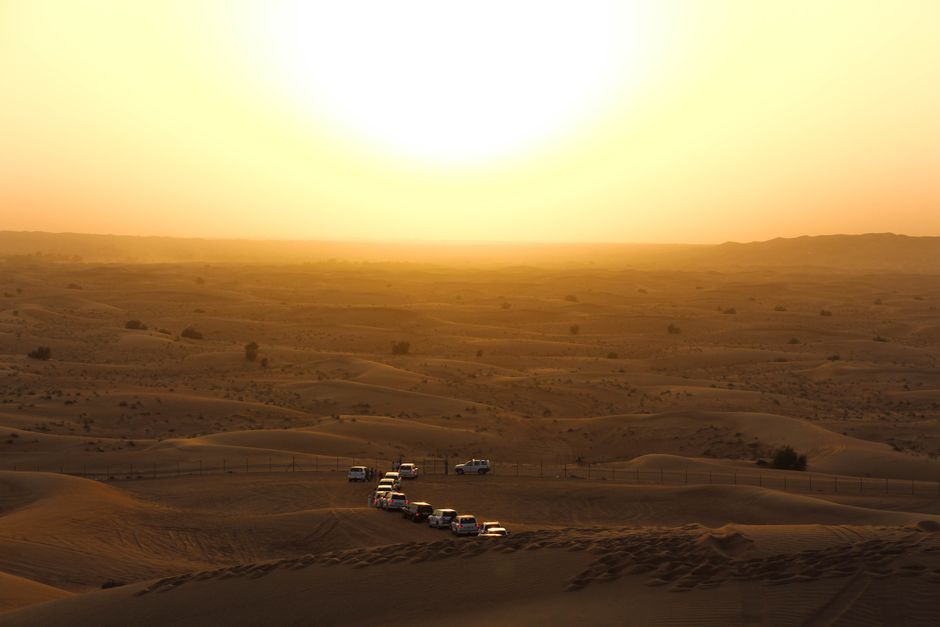 A 4x4 vehicle dune bashing in the Qatar desert at sunset, with the Inland Sea (Khor Al Adaid) in the background