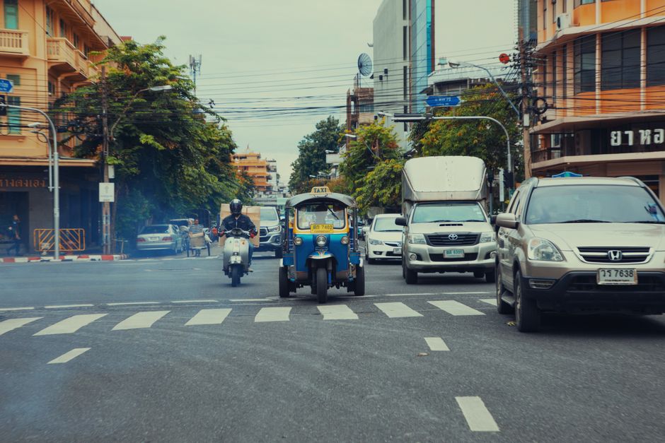 A colorful tuk-tuk driving down a bustling street in Phnom Penh, Cambodia, with local shops in the background.
