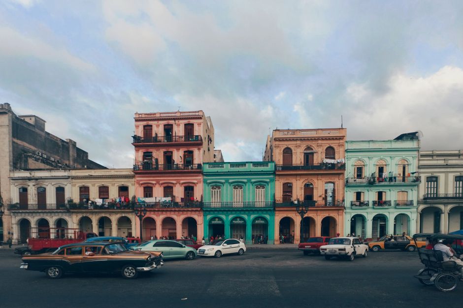 A modern rental car parked next to a classic American car on a vibrant street in Cuba, symbolizing the unique driving experience.
