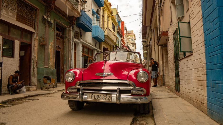 Colorful classic American car (almendrón) driving on a vibrant street in Havana, Cuba, representing local transport for day trips.