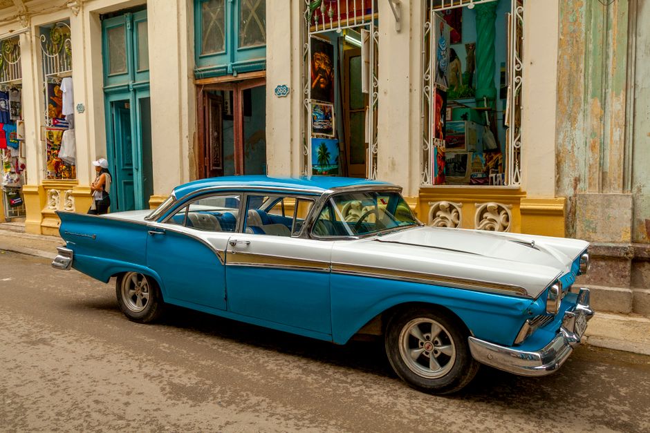 Classic American car, an almendrón, driving down a vibrant street in Havana, Cuba