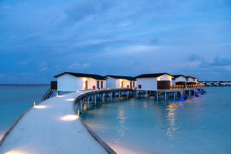Stunning luxury overwater villa at sunset in the Maldives, reflecting clear turquoise waters.