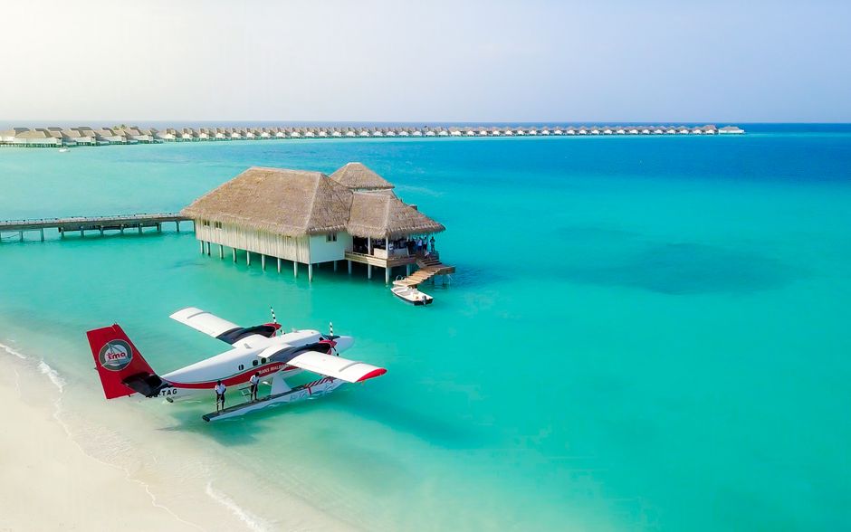 A seaplane flying over a vibrant turquoise lagoon in the Maldives, with luxury resorts visible on small islands below