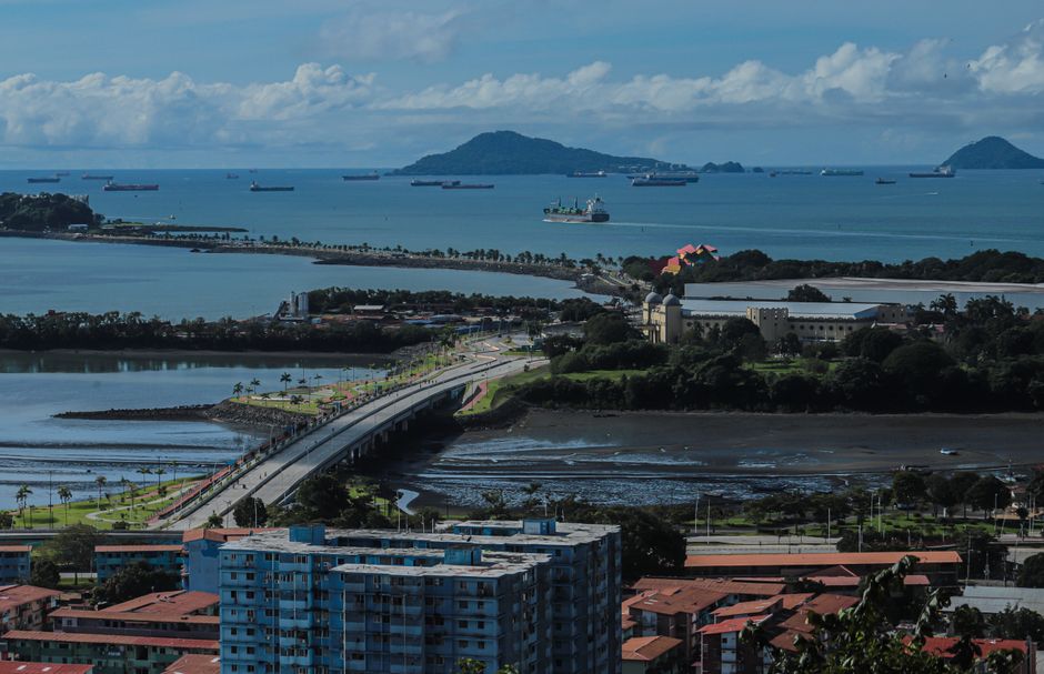 A large cargo ship transiting the Miraflores Locks of the Panama Canal, with lush Panamanian landscape in the background